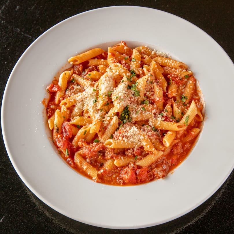 Penne pasta with red sauce, parmesan cheese, and parsley in a white bowl at Mayworth's Public House.