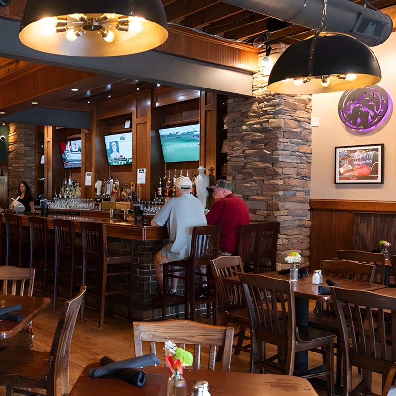Two men sit at the Mayworth's Public House bar, with dining tables and stone pillars in the foreground.