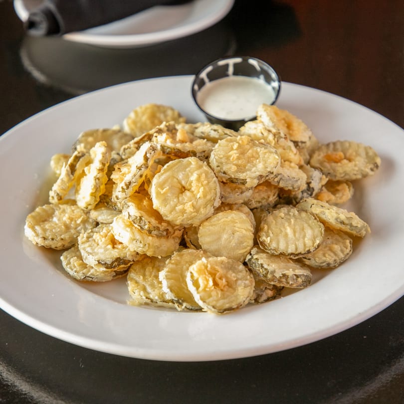 A white plate piled high with golden-brown fried pickles and a side of ranch dressing.