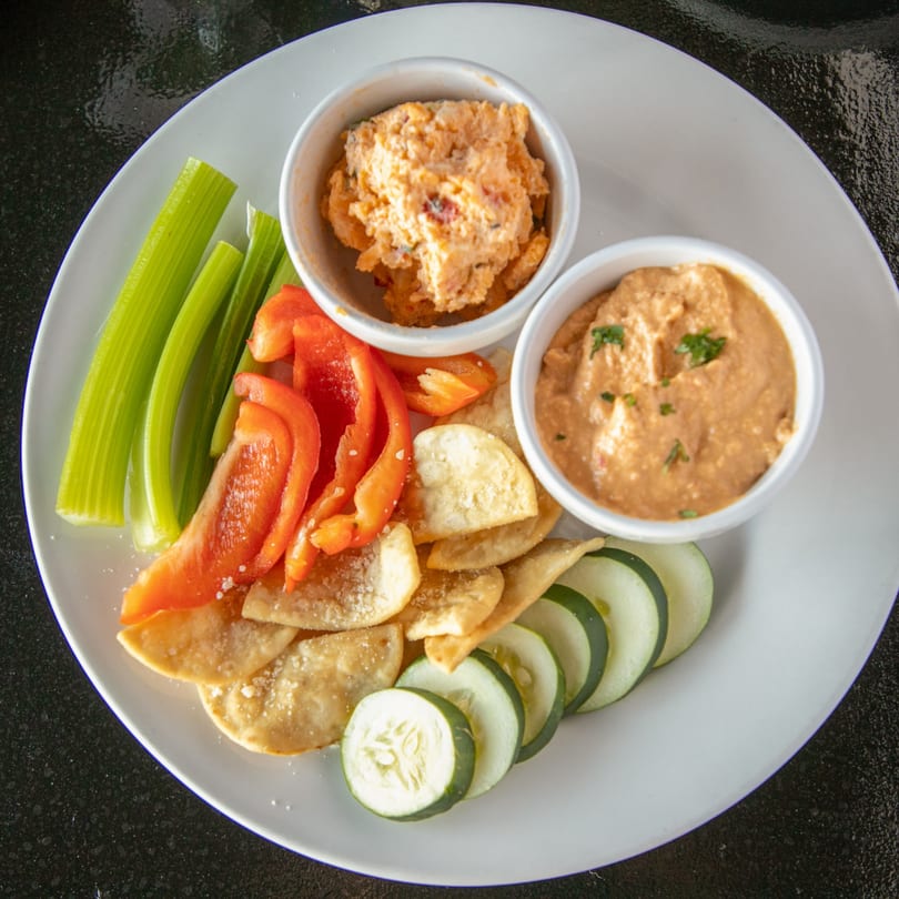 A plate of Mayworth's Public House's hummus and pimento cheese dips with fresh vegetables and pita chips.